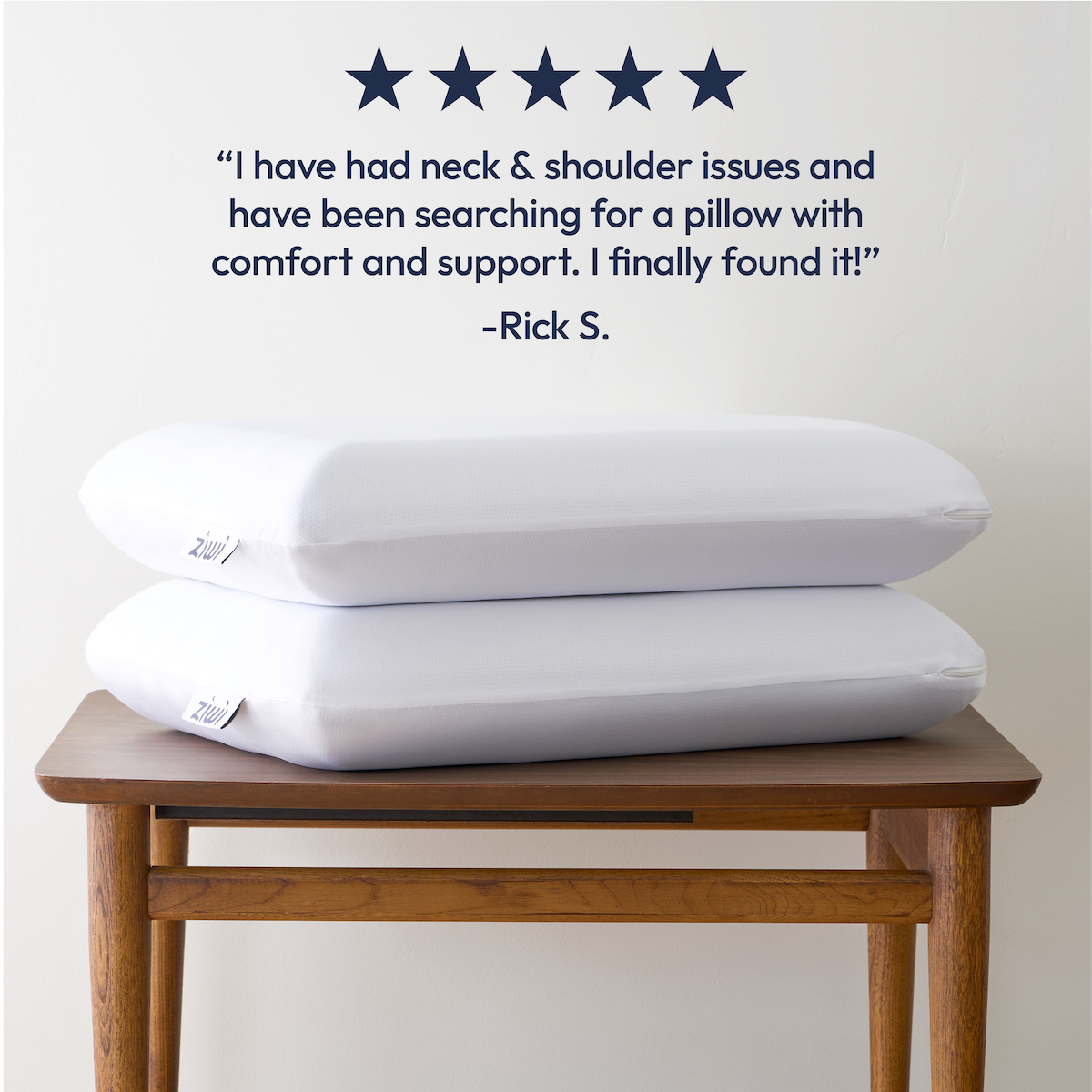 Two white Ziwi ZiPP pillows stacked on a wooden bench with a customer review above them.