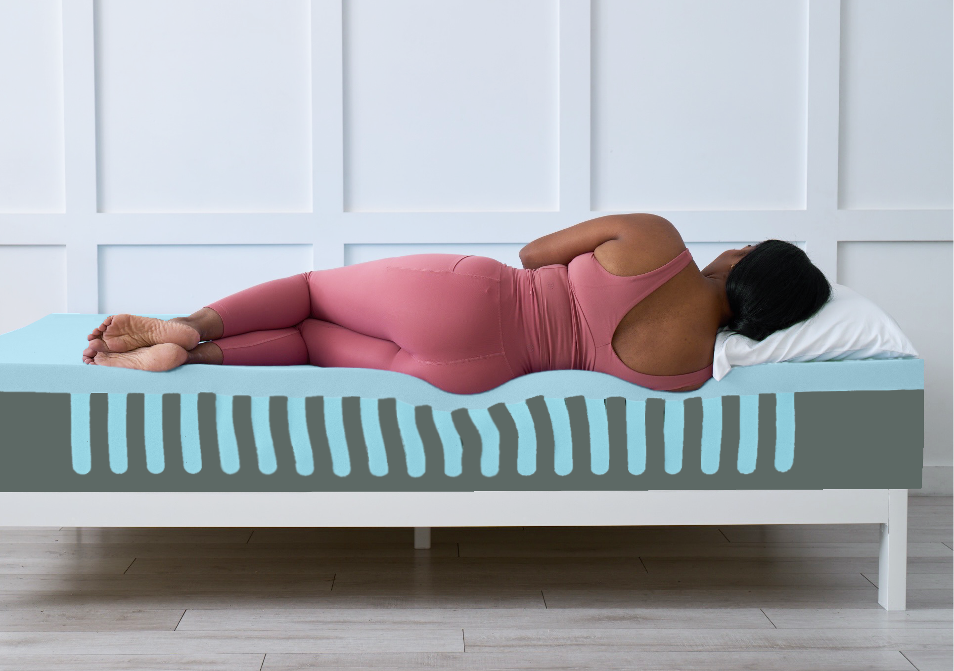 Person lying on a mattress with a white wall and wooden floor in the background