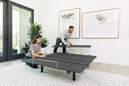 Two people assembling an adjustable bed frame in a modern bedroom.
