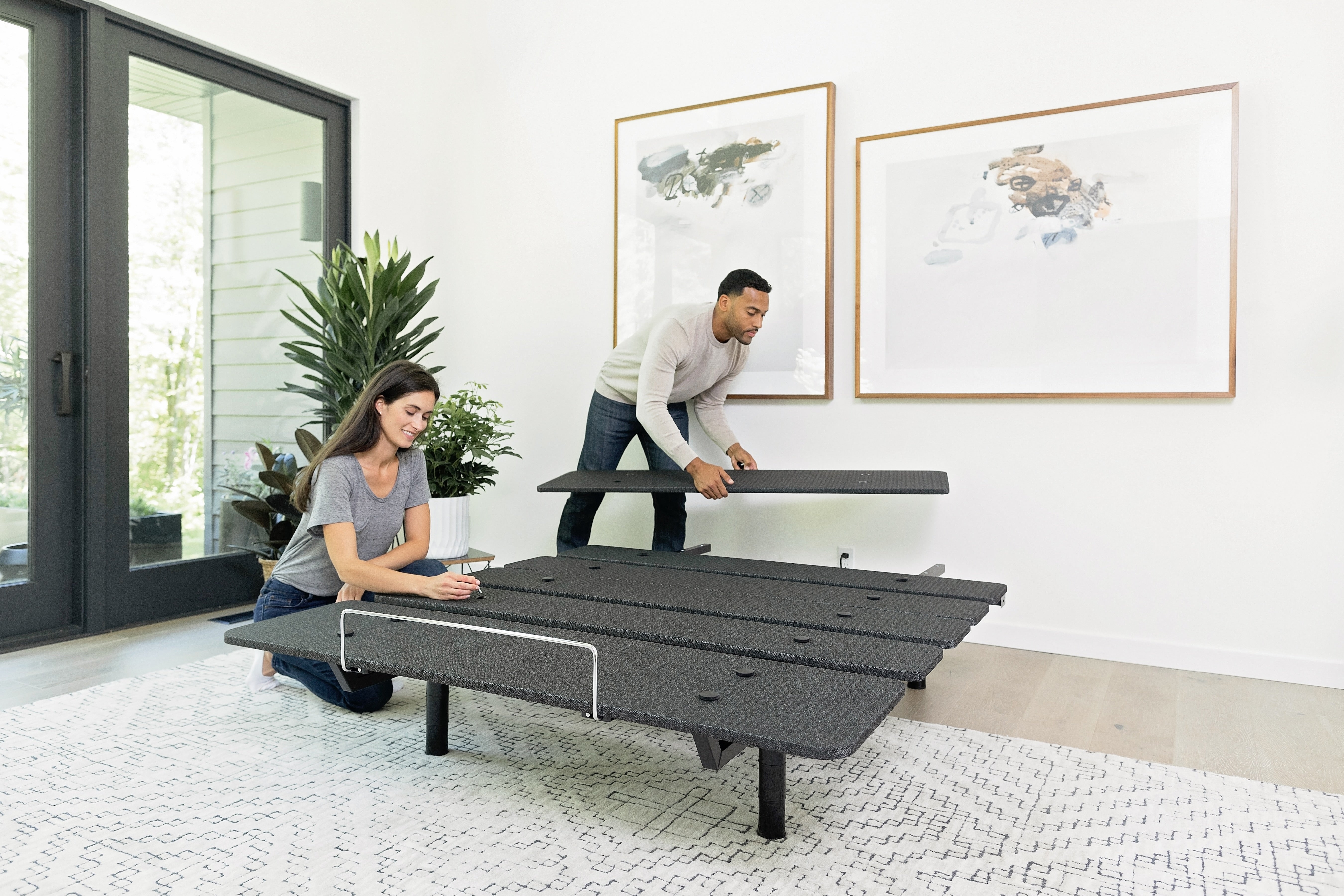 Two people assembling an adjustable bed frame in a modern bedroom.