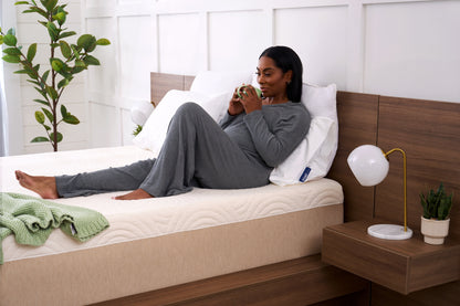 Woman lying on a bed in a modern bedroom with a plant and nightstand.